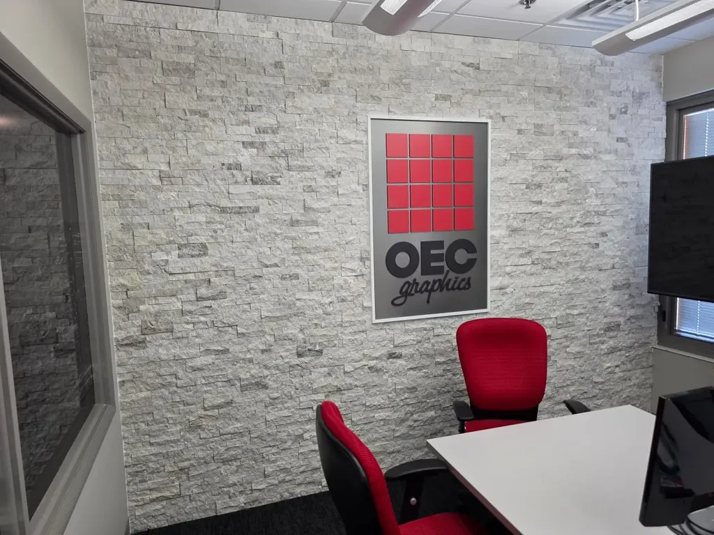Conference room with stone wall, white table, red chairs, and OEC Graphics branding